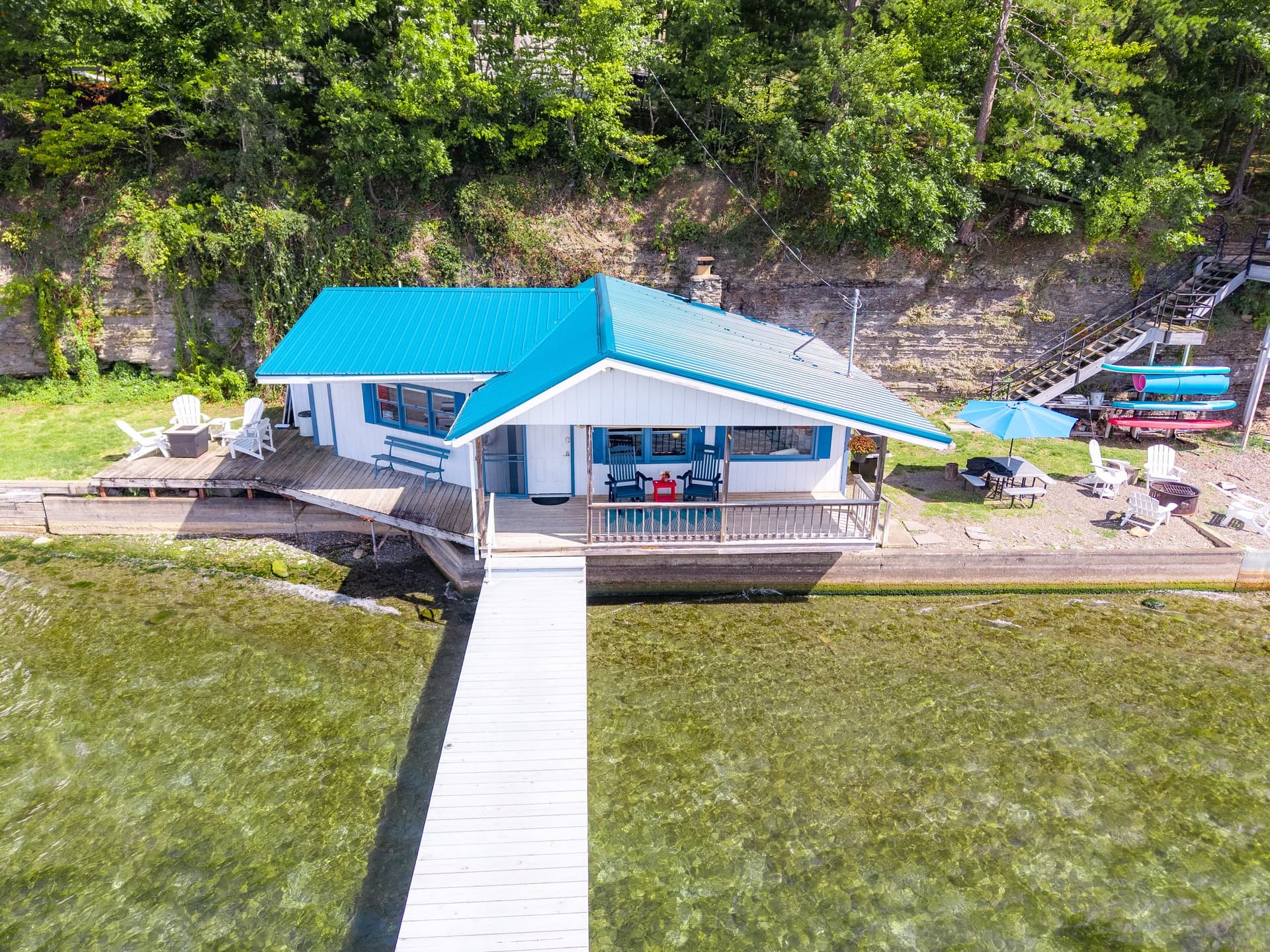 Looking straight down the length of the dock to the cottage, with the shale lake bottom clearly visible through the water on both sides and the green hillside above.