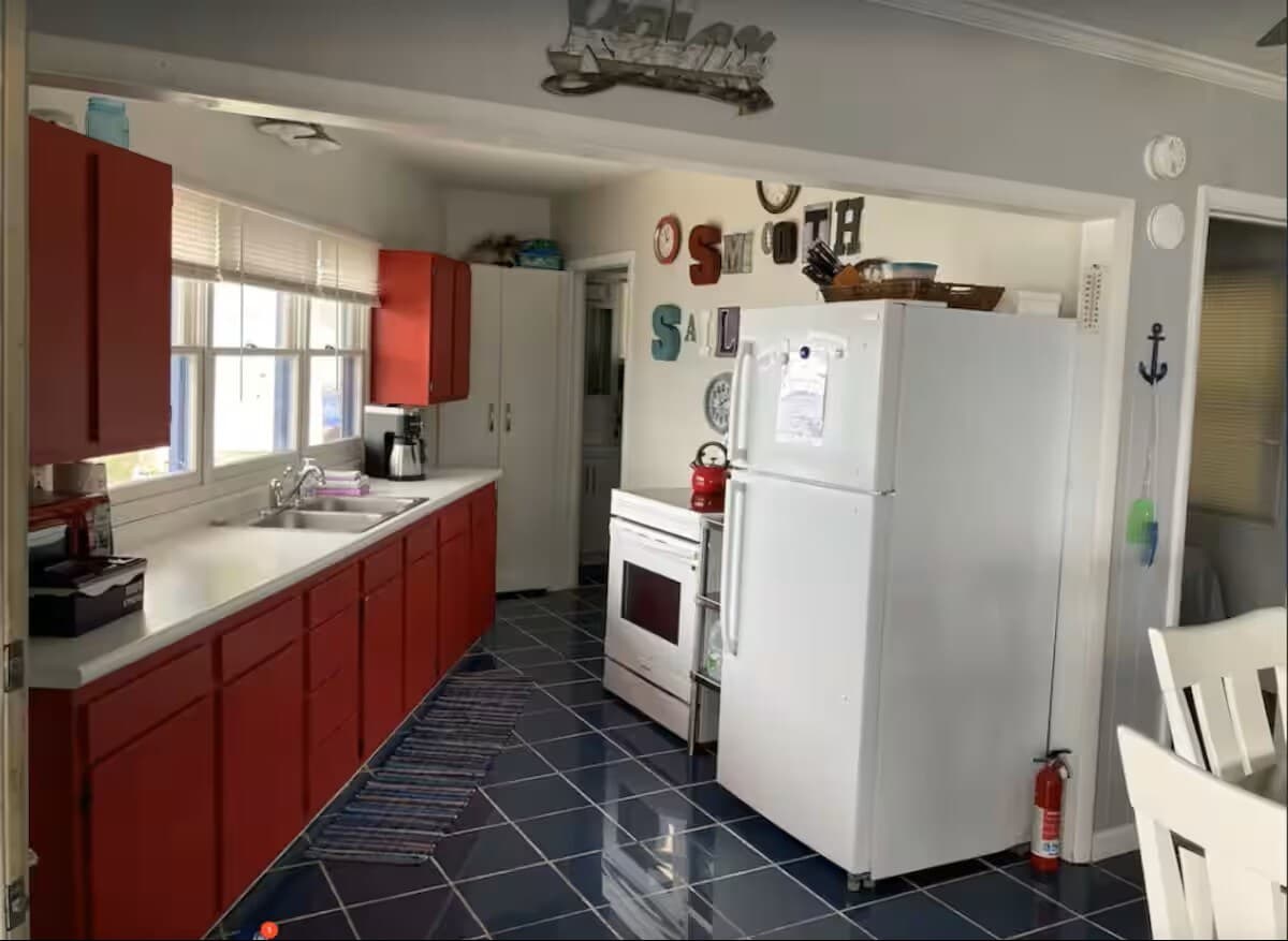 Galley kitchen with red cabinets, a white electric range and refrigerator, and cobalt tile floor.