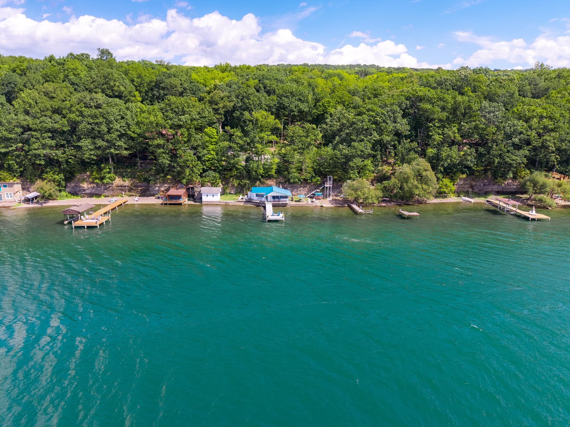 Open Seneca Lake water in deep teal and green under a blue sky with scattered cloud, the wooded east shore running across the upper third.