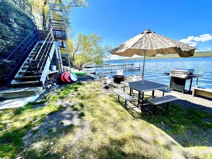 The staircase climbing the shale bluff from the shore, with kayaks and paddleboards stacked at its base and the picnic table and grill on the terrace beyond.